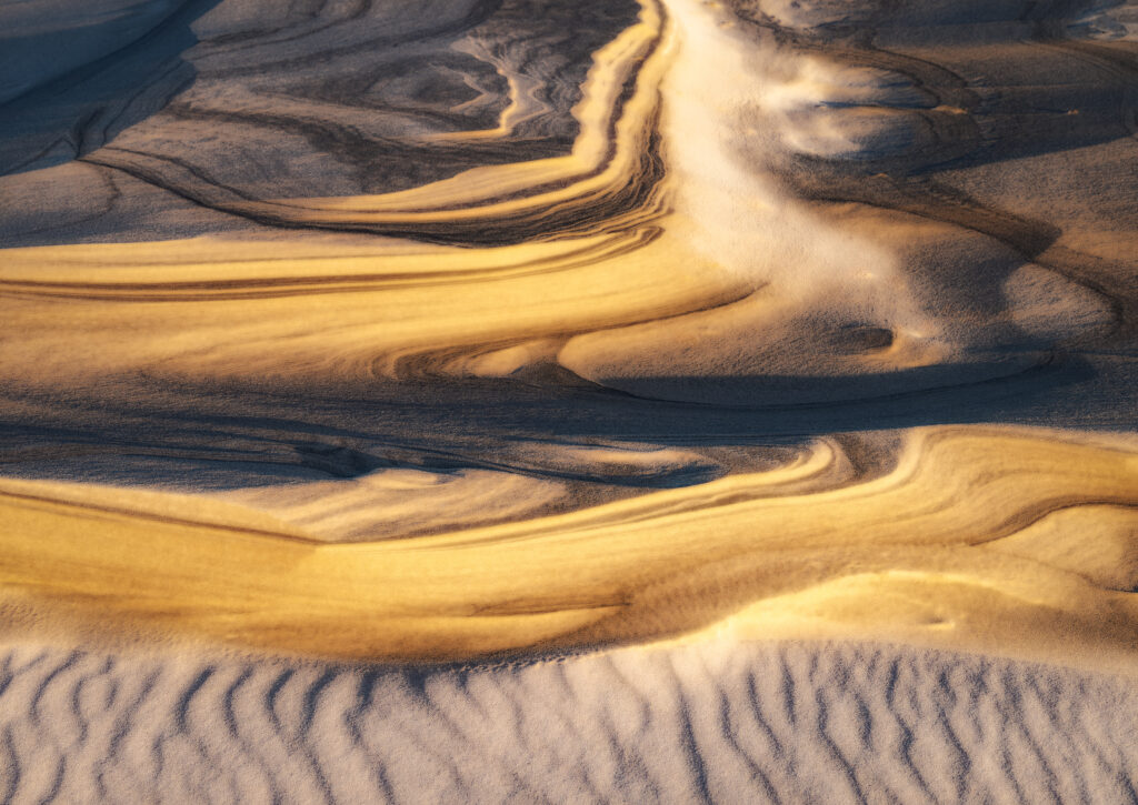 Golden sunlight on rippled sand dunes with flowing relief lines and rich ochre shadows background Wallpaper