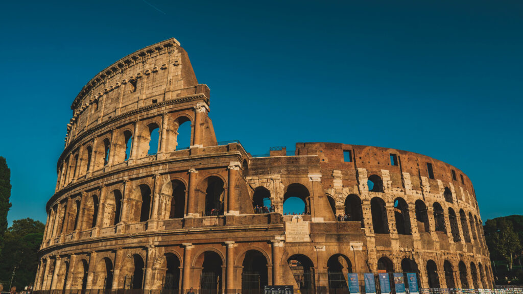 Golden sunlight illuminates Rome's Colosseum against a deep blue sky wallpaper background