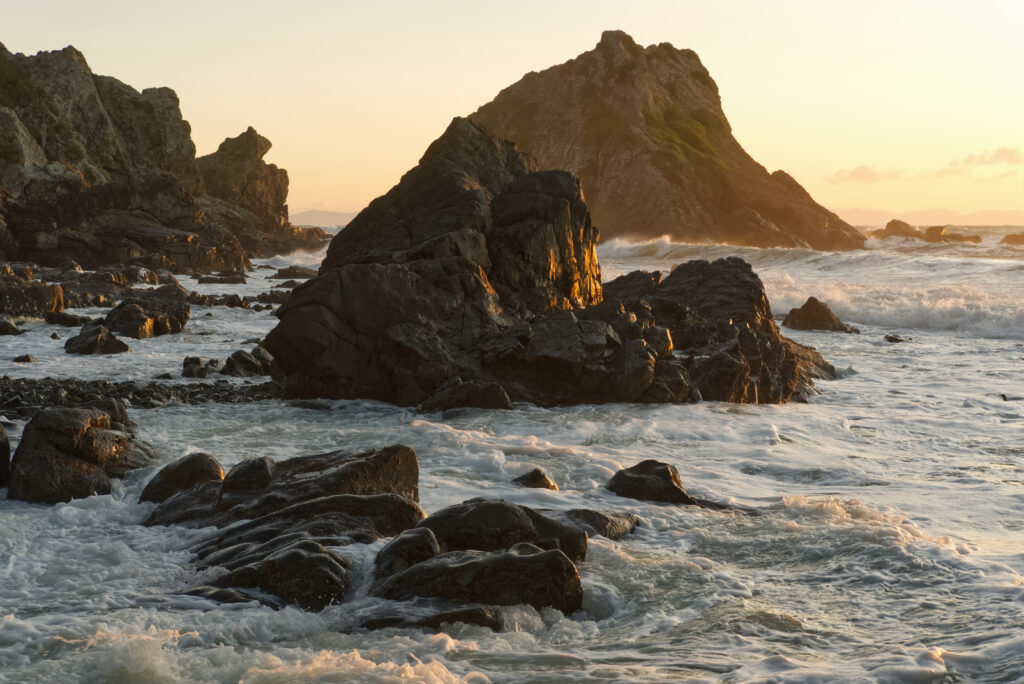 Golden sunlight on rugged coastal rocks with swirling sea foam in a tranquil shoreline scene Wallpaper