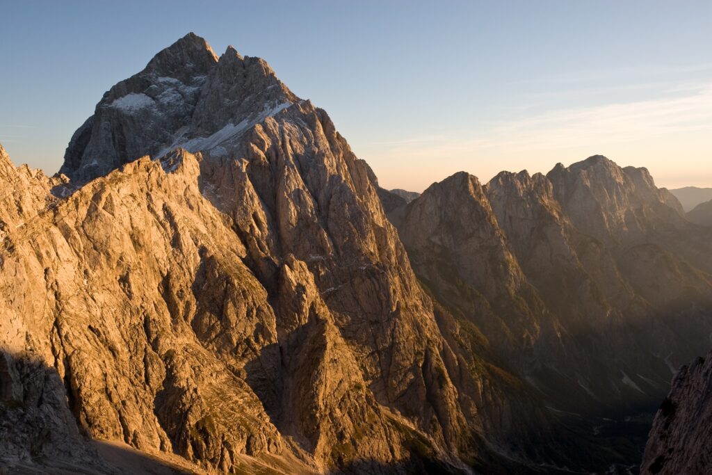 Golden sunlight illuminates rugged mountain peaks under clear morning sky with warm shadows Wallpaper