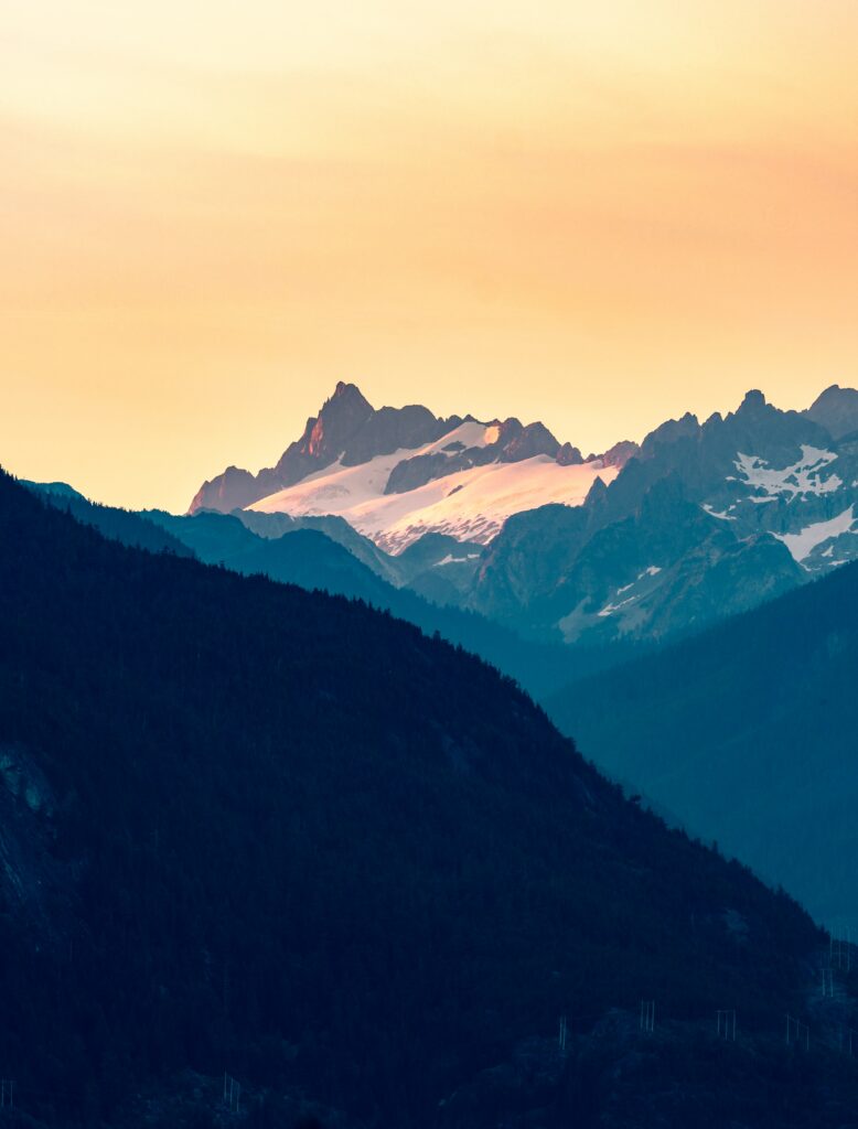 Golden sunlight on Canadian snow-capped mountains with blue foothills and clear sky landscape Wallpaper