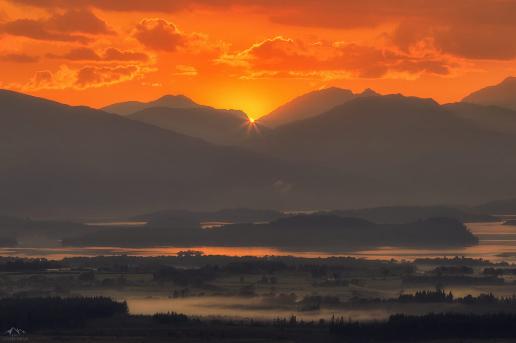 Golden sunlight over Scottish mountains with misty lakes and vibrant orange red sunset colors Wallpaper