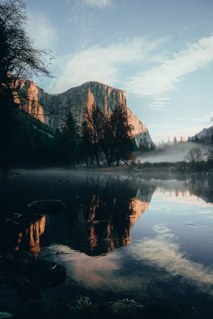 Serene autumn landscape with golden sunlight rock cliff misty fog calm reflective water wallpaper