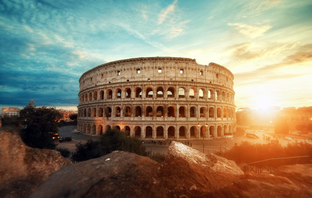 Colosseum in golden sunlight under blue sky with soft clouds historic Roman architecture wallpaper