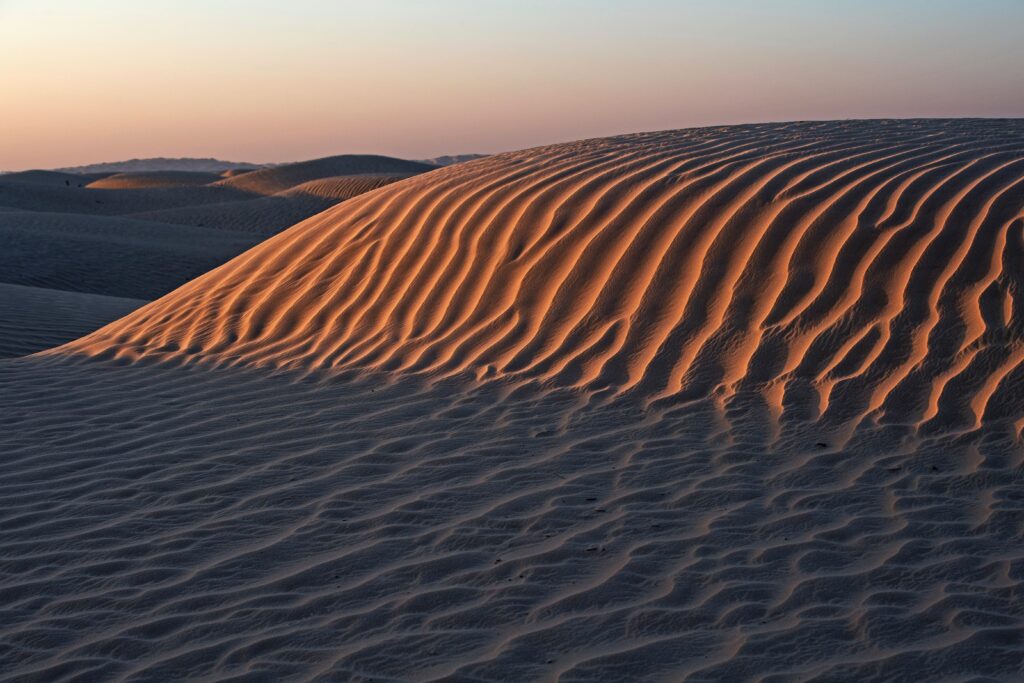Golden sunlight on rippled desert sand dunes and rolling hills with warm and cool tones background Wallpaper