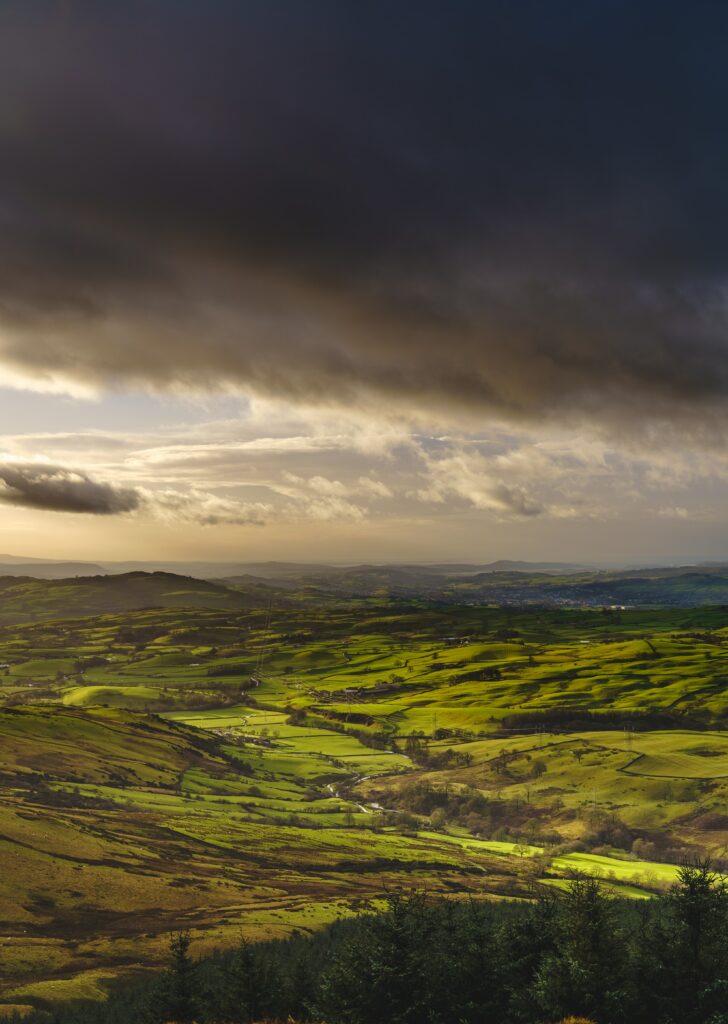 Lush green valley with golden sunlight and dramatic clouds creating moody countryside views Wallpaper