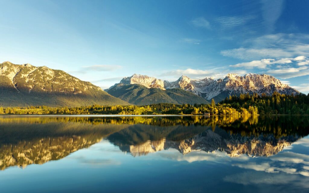 Golden sunlight on rugged mountains reflecting in calm lake under vivid blue sky wallpaper