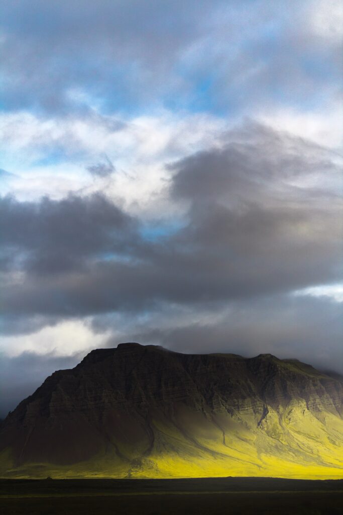 Dramatic mountain landscape with rugged peaks in golden sunlight under moody cloudy sky background Wallpaper