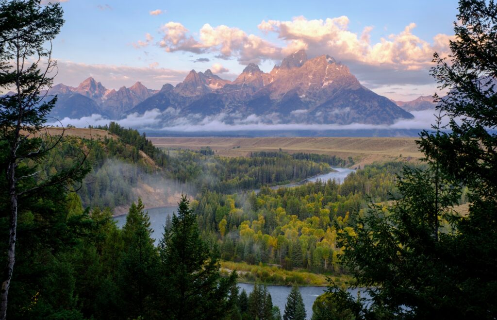 Towering mountains in golden sunlight with winding river dense green forests and morning fog Wallpaper