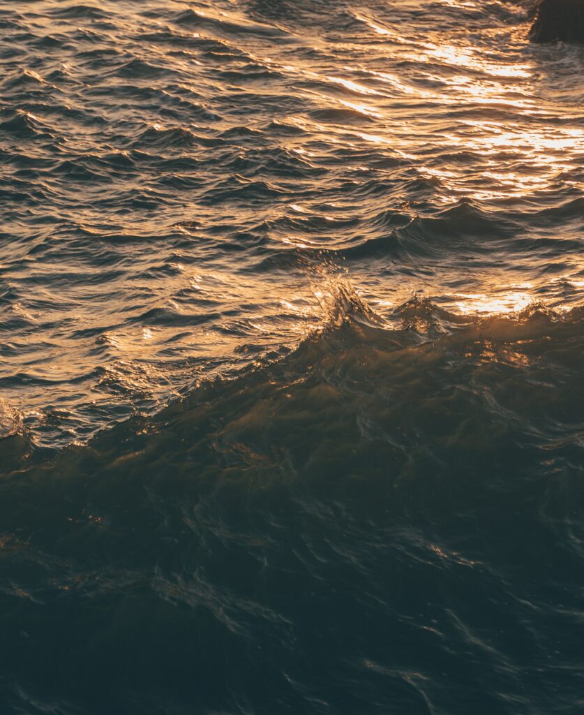 Dynamic ocean waves with golden sunlight reflections creating a serene blue sea wallpaper background