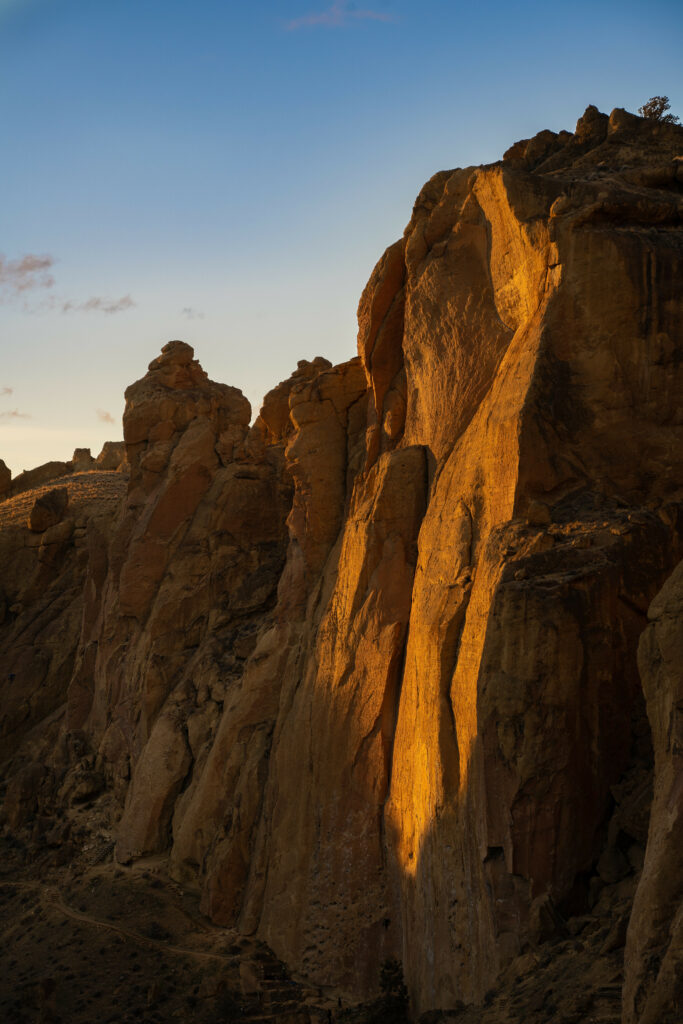 Golden sunlight illuminates towering rugged rock cliffs with warm earthy tones under clear sky Wallpaper