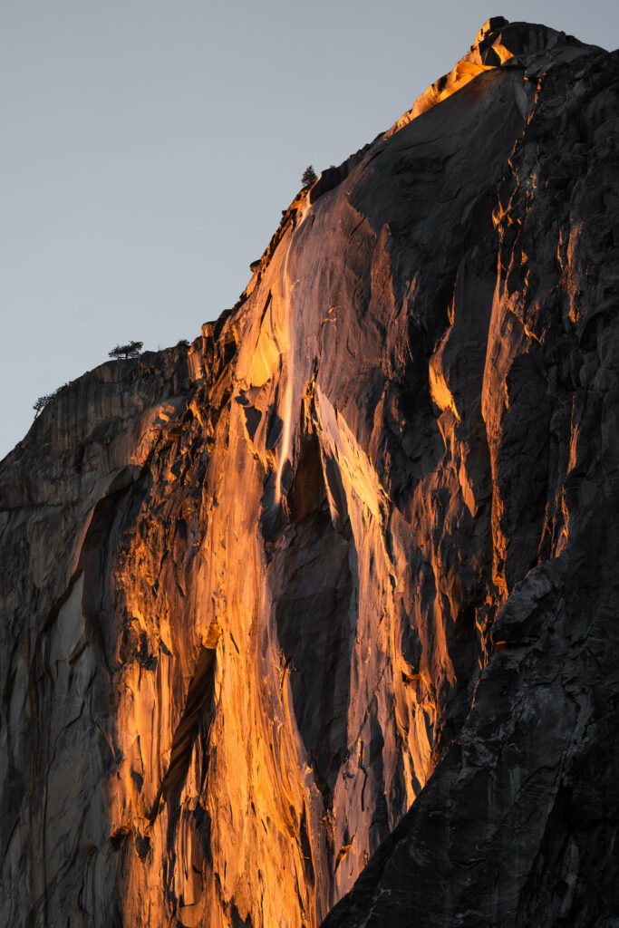 Majestic sunlit rock face with textured cliffs and sparse vegetation in serene nature landscape Wallpaper