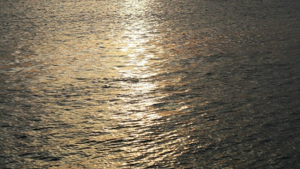 Golden sunlight reflecting on gentle ocean ripples minimalist serene sea wallpaper background