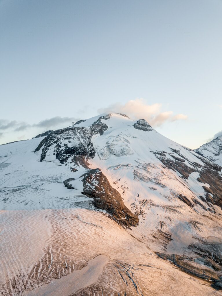 Snowy mountain landscape with golden sunlight on slopes under clear blue sky wallpaper background