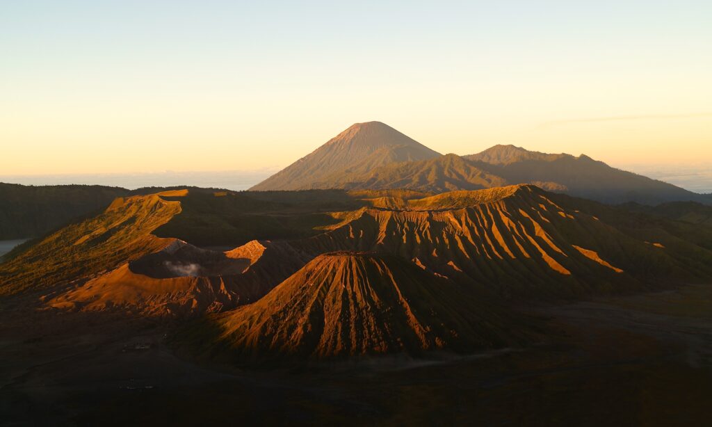 Golden sunlight illuminates volcanic peaks and rugged mountains under a clear blue sky wallpaper