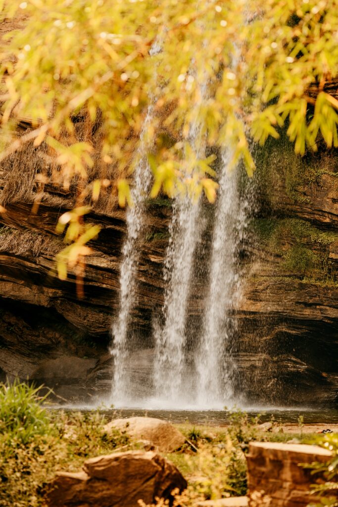 Tranquil waterfall cascading over rocks with lush green plants golden sunlight wallpaper