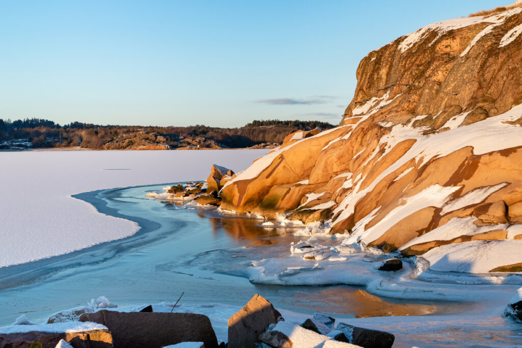 Winter landscape wallpaper with snow-covered rocks and a frozen river glowing in warm sunlight
