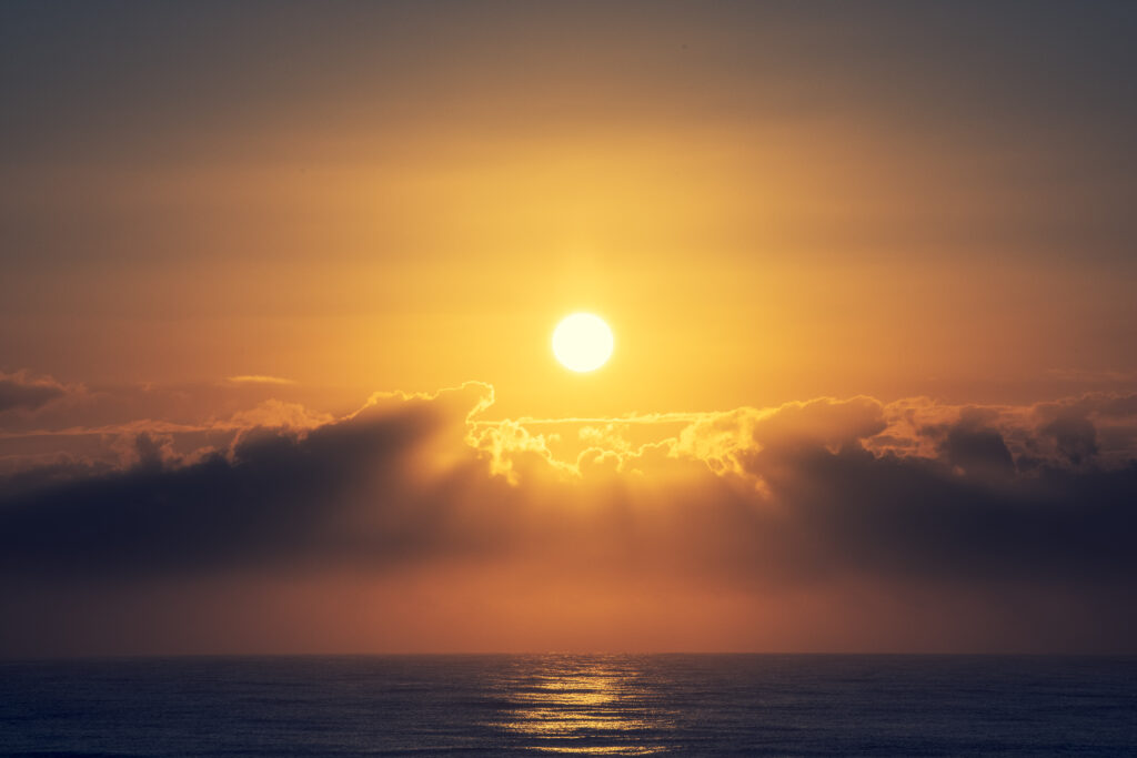 Golden sunrise over calm sea with soft glowing clouds and gentle waves peaceful wallpaper