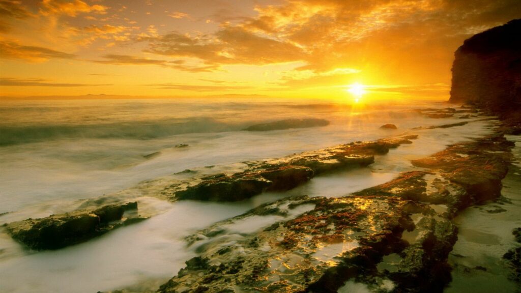 Golden sunrise over foggy sea with rugged shoreline stones in warm dreamy coastal dawn wallpaper