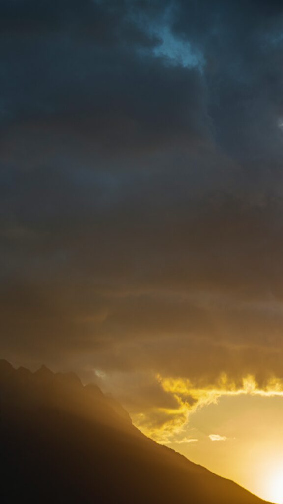 Rugged mountain slopes glowing in sunrise light beneath dramatic clouds vibrant sky background Wallpaper