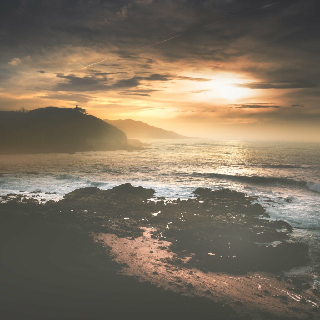 Sunrise over rugged mountains and calm sea with golden light on rocky shores and waves Wallpaper