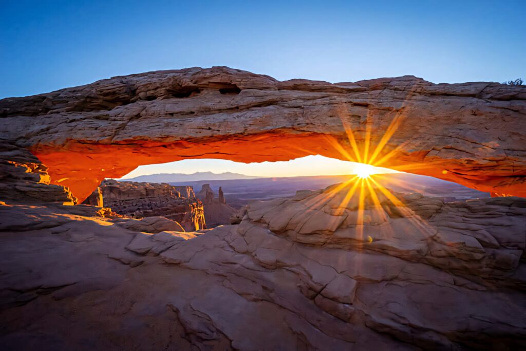 Sunrise under Delicate Arch glowing golden on sandstone textures with clear blue sky background Wallpaper