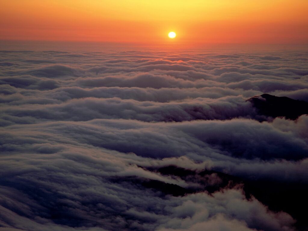 Breathtaking sunset above soft clouds with warm golden hues creating a serene sky view Wallpaper