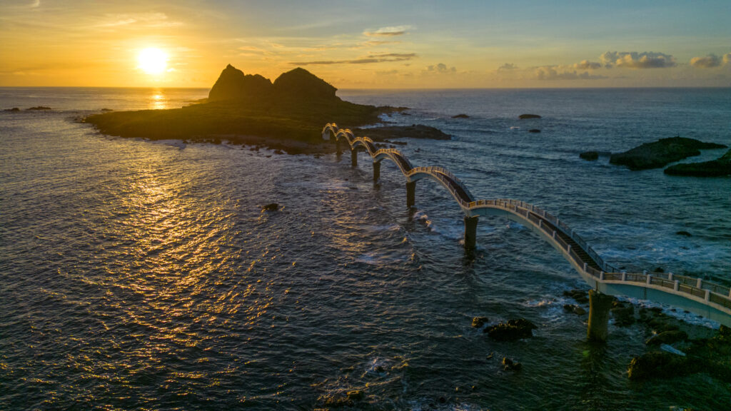 Graceful bridge over shimmering sea with rugged mountains at vibrant sunset sky wallpaper background