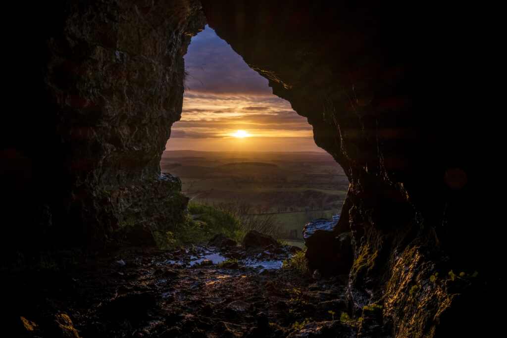 Sunset through cave entrance lighting rolling hills and fields peaceful natural landscape wallpaper