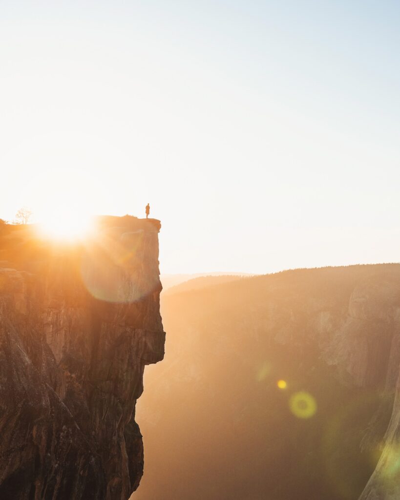 Lone silhouette on towering cliff edge in golden sunlight with warm sky and lens flare wallpaper