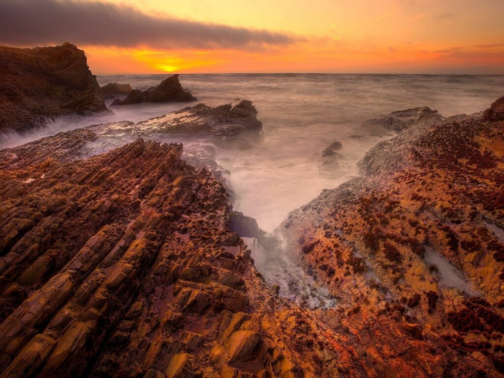 Sunset coastal landscape with mossy rocks rugged stone blocks foggy seaside and golden sky Wallpaper
