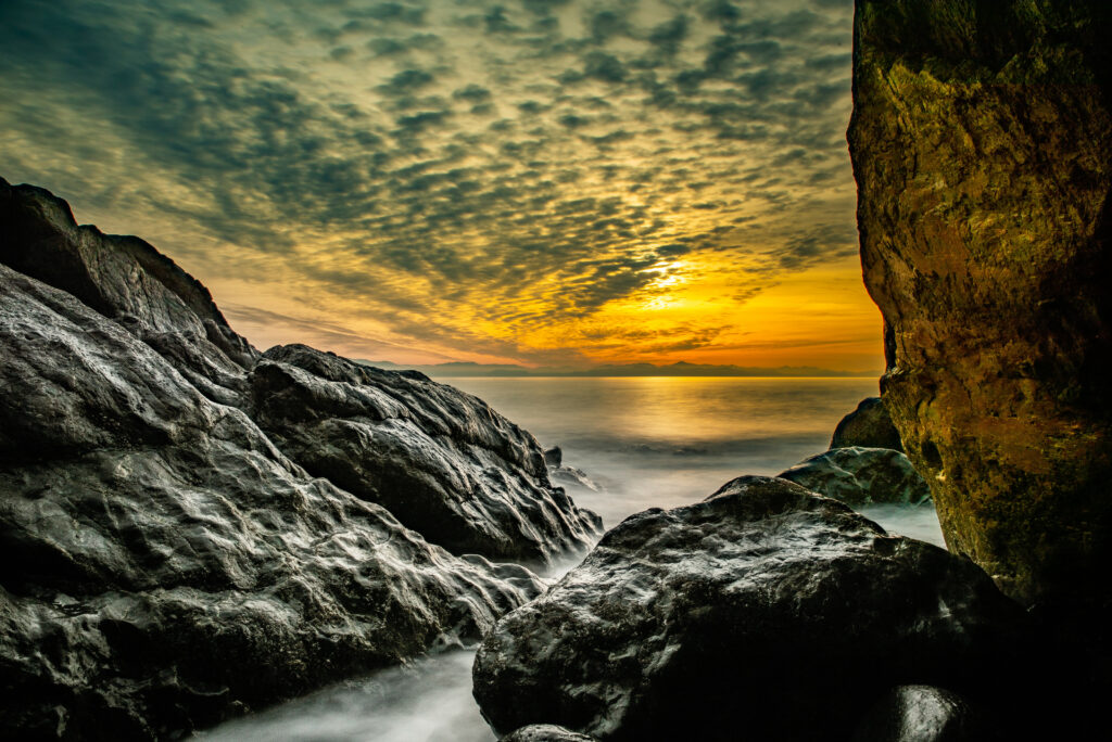 Sunset coastal wallpaper with rugged rocks golden light dramatic sky and calm sea horizon