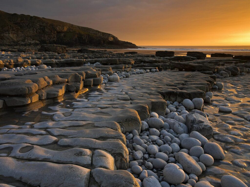 Sunset coastal wallpaper with unique stone formations smooth rocks golden light calm sea cliffs