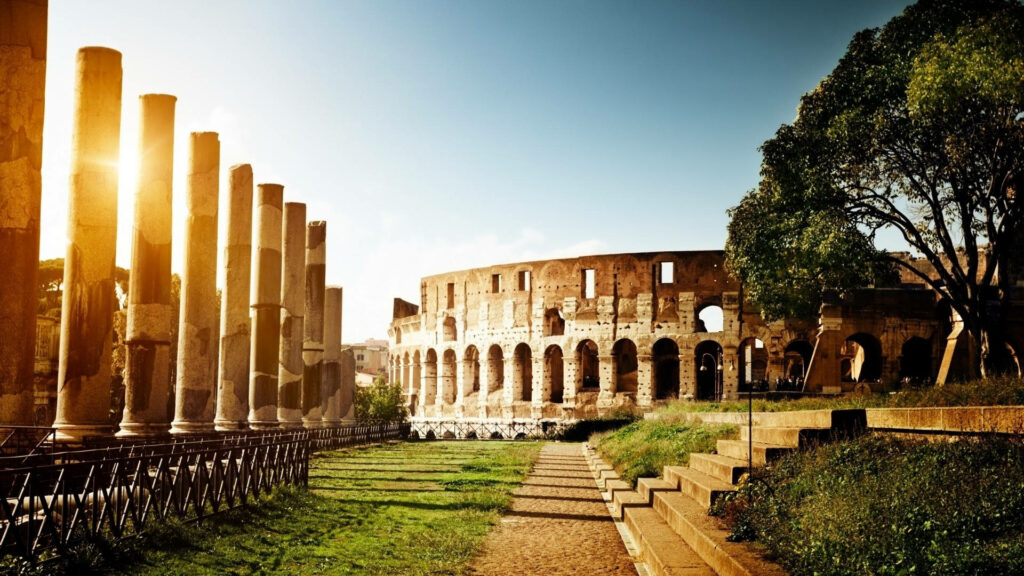 Majestic Colosseum at sunset with golden light ancient pillars and lush greenery in Rome Wallpaper