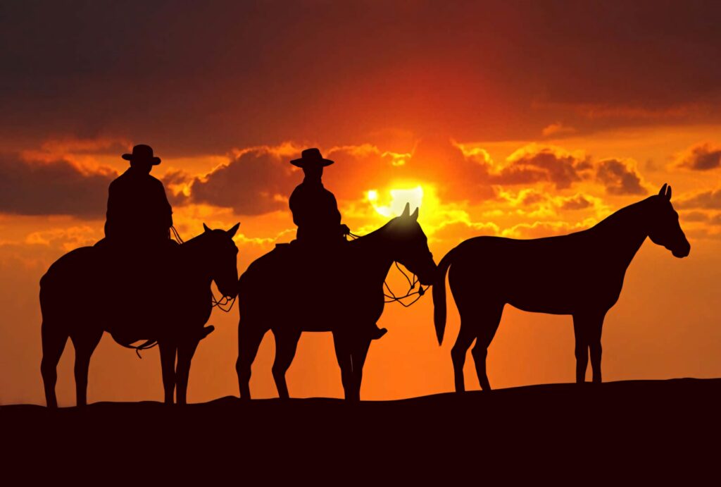 Three cowboys silhouetted on horseback ride against a vibrant golden sunset Western sky wallpaper