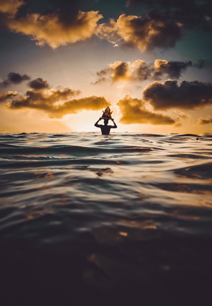 Silhouette of devotee holding Lord Ganesha idol over ocean at golden sunset Ganesh Visarjan wallpaper