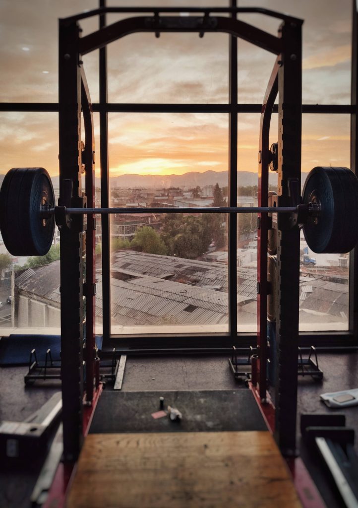 Loaded barbell on power rack with golden sunset over mountain cityscape fitness wallpaper background