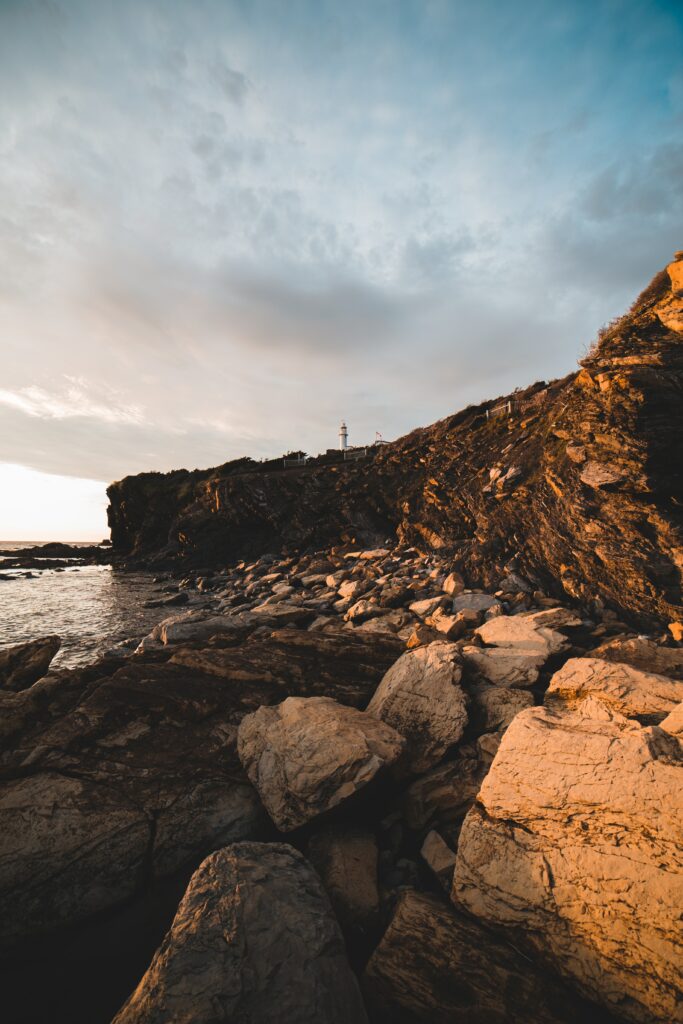 Lighthouse on rugged cliff with textured rocks under warm golden sunlight coastal wallpaper background