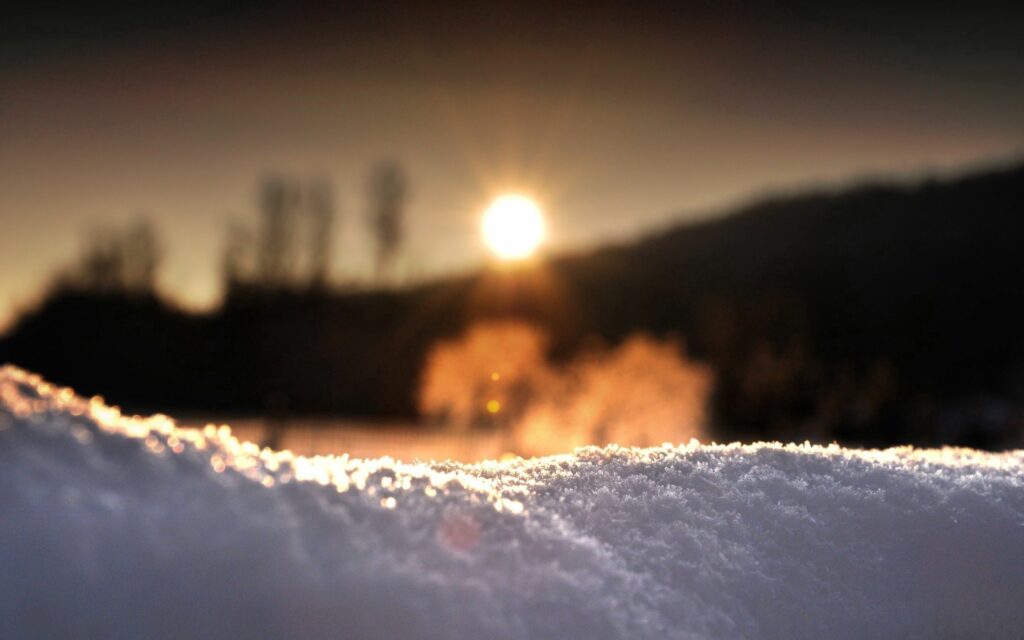 Macro close-up of sparkling snow grains glowing golden at sunset over blurred winter landscape Wallpaper