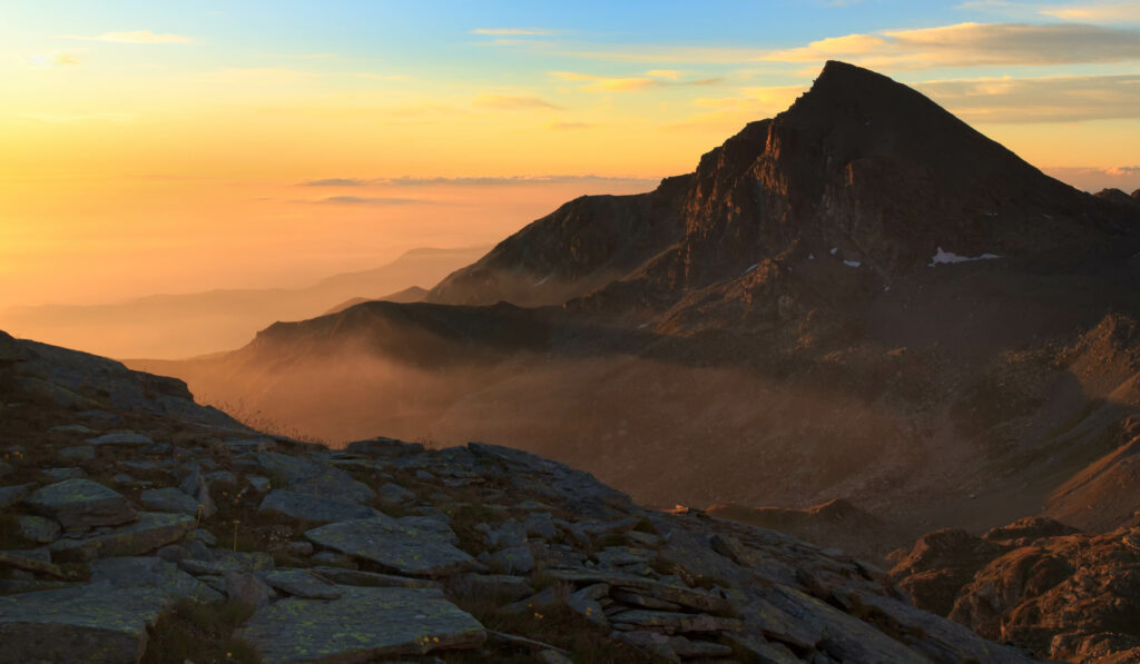 Mountain landscape wallpaper with golden sunset light misty layers and dramatic craggy rocks