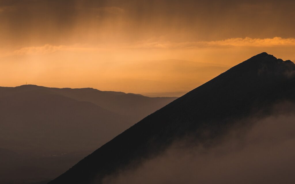 Golden sunset behind foggy mountain peak with soft orange sky and tranquil misty layers Wallpaper