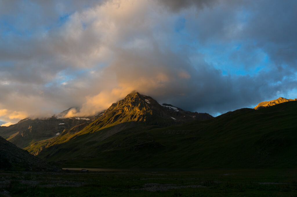Dramatic mountain peak with rocky summit and golden clouds above green sunlit slopes wallpaper