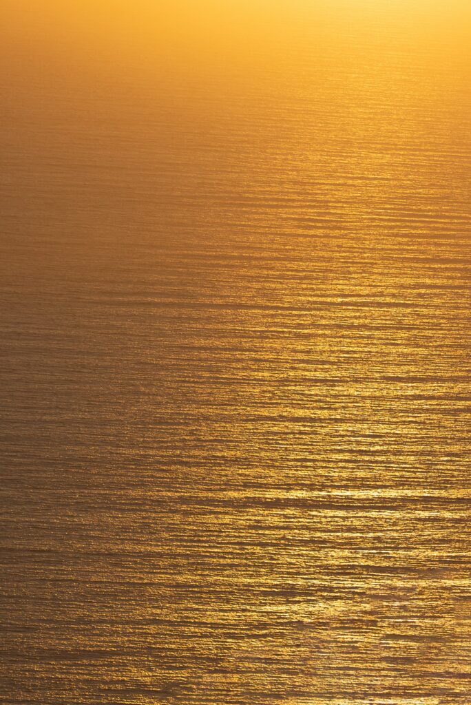 Aerial ocean view at sunset with golden light reflecting on gentle ripples and waves wallpaper