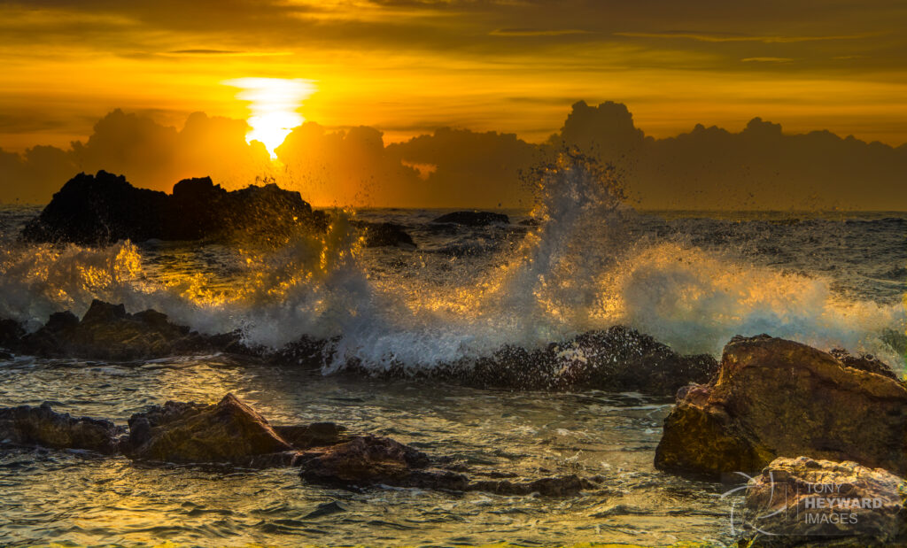 Golden sunset over ocean waves crashing on jagged rocks with vibrant colorful sky background Wallpaper