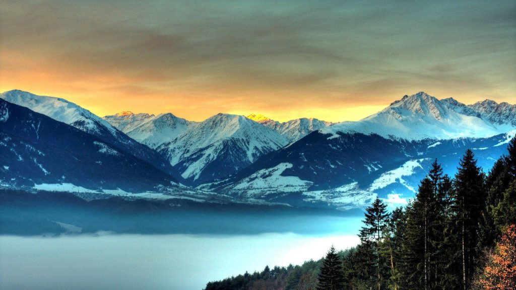 Snow-capped alpine mountains with golden sunset valley fog and pine forest high-definition wallpaper