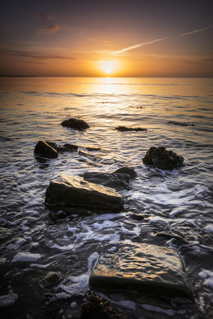 Sunset over calm coastal water with golden light rocks soft clouds and serene reflections wallpaper