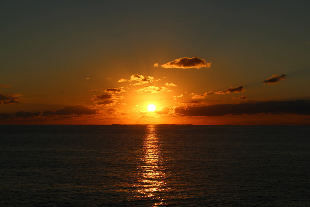 Sunset wallpaper with glowing sun setting over calm ocean casting warm orange golden hues
