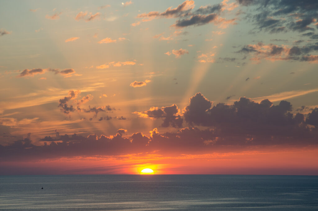 Sunset over calm sea with golden orange hues and dramatic rays breaking through clouds wallpaper