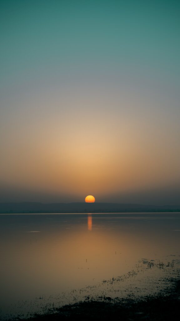 Golden sunset over calm sea with warm horizon hues and clear water reflection wallpaper background