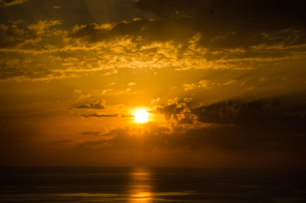 Sunset over calm sea with golden glow warm orange sky and scattered clouds coastal wallpaper